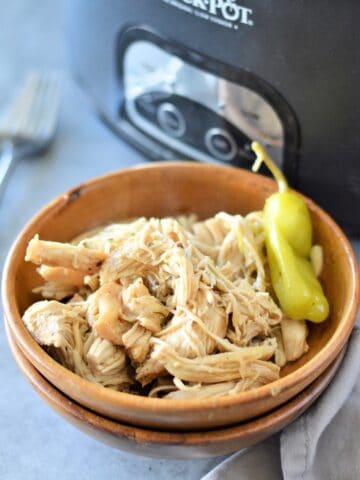 cooked mississippi chicken in bowl with crockpot in background